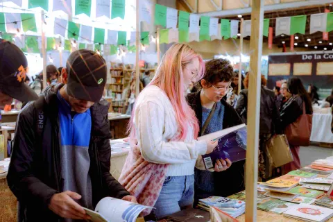 Visitors browse and explore books at a literary fair booth, amidst a cultural setting filled with passionate readers, publishers, and literary activities.