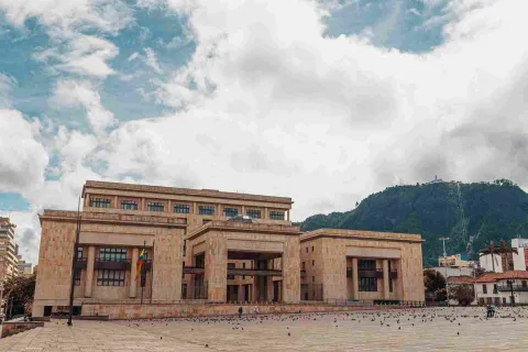 De frente, fachada de estructura con tres edificaciones en piedra. Sobresalen al fondo los cerros orientales de Bogotá.