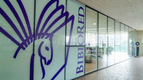 A library facade with glass walls and a purple hummingbird graphic design, identifying the space as a modern and cultural venue.
