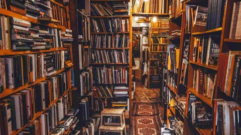 Narrow bookstore aisle with shelves overflowing with books and warm light creating a cozy atmosphere.