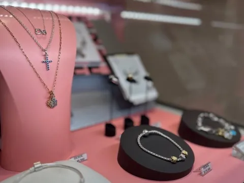  Exhibición de joyería con collares y pulseras sobre soportes rosados y negros en una vitrina de tienda.