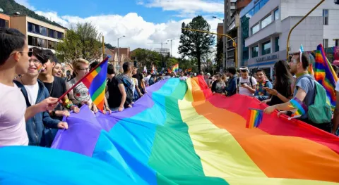 Personas participan en una marcha del orgullo LGBTQ+ sosteniendo una gran bandera arcoíris en una calle de Bogotá.