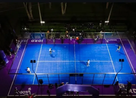 Vista aérea de una cancha de pádel durante un partido en desarrollo, donde los jugadores compiten en un escenario moderno iluminado y rodeado de graderías.
