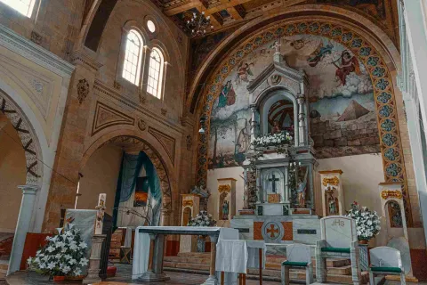  Interior de iglesia en la que sobresale un atrio con mantel blanco y arreglos florales con flores blancas.