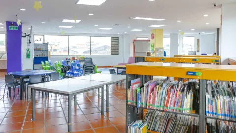 Children's library room with bookshelves, work tables, and colorful chairs in a spacious and bright area for reading and learning.