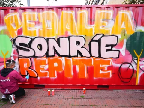 Persona realiza un grafiti con el mensaje “Pedalea, sonríe, repite” sobre un contenedor urbano en Bogotá.