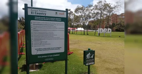 Aviso informativo del Parque Público El Country en primer plano, con amplias zonas verdes, árboles y el logo del IDRD visibles al fondo.