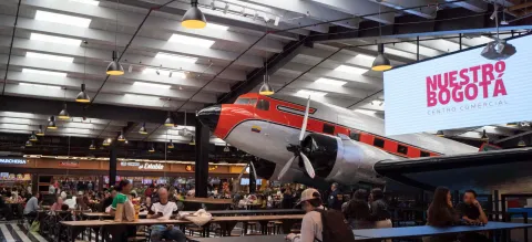 Interior of the Nuestro Bogotá shopping mall with a food court and a vintage airplane displayed as a central attraction.