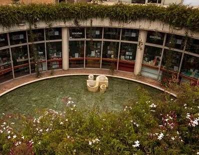 Patio interior del Centro Cultural Gabriel García Márquez, con un espejo de agua circular rodeado de jardines floridos y locales de la librería del Fondo de Cultura Económica. La arquitectura curva de ladrillo y concreto enmarca el espacio, característico del diseño de Rogelio Salmona.