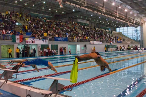 Nadadores se lanzan desde los bloques de salida durante una competencia en el Complejo Acuático de Bogotá, ante la mirada de cientos de espectadores que llenan las graderías de este escenario deportivo de nivel internacional.