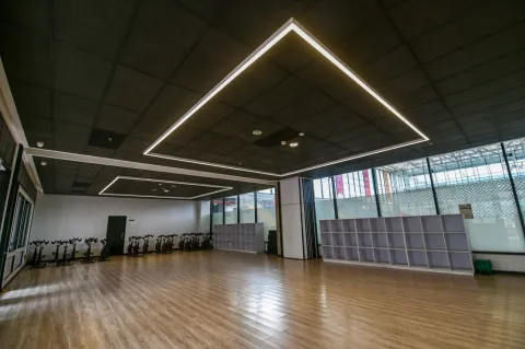 Salón multifuncional del Centro Felicidad (CEFE) El Tunal, diseñado para actividades deportivas y recreativas. El espacio destaca por su amplitud, piso de madera, iluminación moderna y ventanales que permiten la entrada de luz natural, ofreciendo un ambiente cómodo para clases grupales y entrenamiento físico.