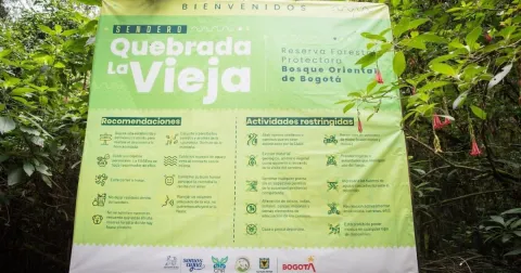 Aviso informativo del sendero Quebrada La Vieja, ubicado en la Reserva Forestal Protectora Bosque Oriental de Bogotá. El letrero, rodeado de vegetación, presenta recomendaciones para los visitantes y normas de conservación para proteger este entorno natural.
