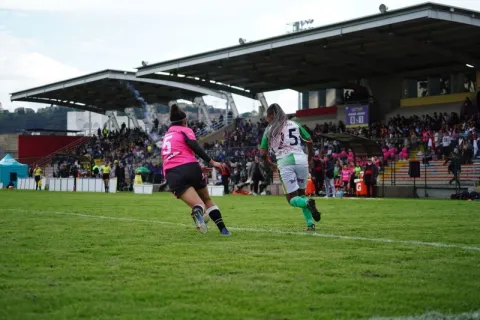 Dos futbolistas disputan una jugada en la cancha del Estadio Olaya Herrera, con las graderías llenas de espectadores durante un partido.