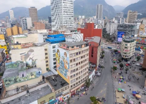 Vista panorámica del sector de San Victorino y el centro de Bogotá, con edificios comerciales, coloridos murales y una concurrida avenida. Al fondo se elevan los Cerros Orientales, enmarcando uno de los principales corredores comerciales y urbanos de la capital.