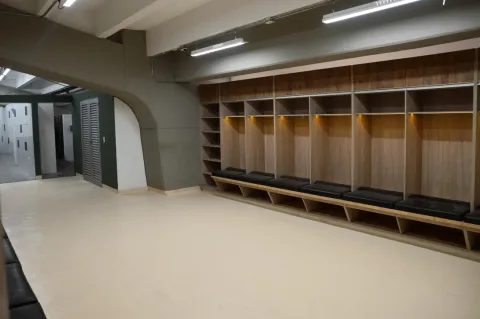 Vestuario del Estadio de Techo con casilleros de madera, bancas acolchadas y acceso a las duchas, en un espacio amplio e iluminado.