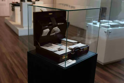  Maletín antiguo con documentos y cheques históricos, protegido por una vitrina de vidrio y exhibido como pieza museográfica.