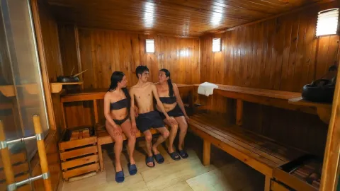 Sauna de madera con tres personas disfrutando de un momento de relajación y bienestar en un ambiente cálido y acogedor.
