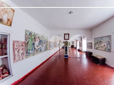 Sala de museo con piso de baldosas rojas y paredes blancas, donde se exhiben pinturas y obras de arte a lo largo de un amplio corredor con arcos.