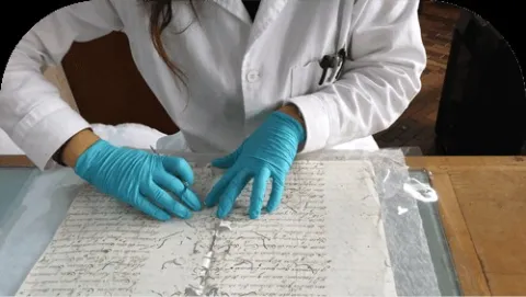 Especialista en conservación documental revisando cuidadosamente un manuscrito histórico con guantes.