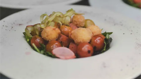 Plato hondo de cerámica blanca con una ensalada gourmet compuesta de tomates cherry, esferas apanadas y vegetales.