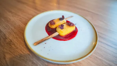 Dos paletas heladas de fruta sobre salsa roja brillante decoradas con flores comestibles en un plato blanco.