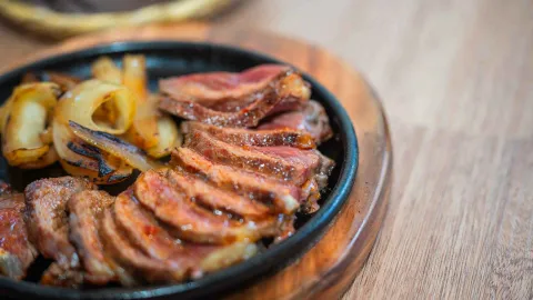 Medallones de carne de res jugosa tajados y servidos con cebollas asadas en un plato caliente de hierro.