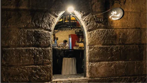 Una entrada de arco de piedra iluminada en una pared de bloques de piedra rústica, revelando un interior de bar acogedor.