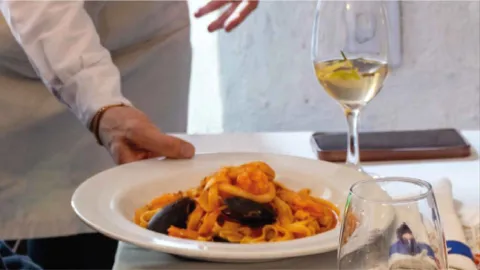 Un plato de pasta con mariscos, incluyendo mejillones y gambas en salsa roja, servido en una mesa con una copa de vino.