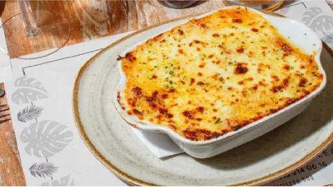 Fuente refractaria de cerámica con lasaña horneada y queso dorado gratinado en la superficie.