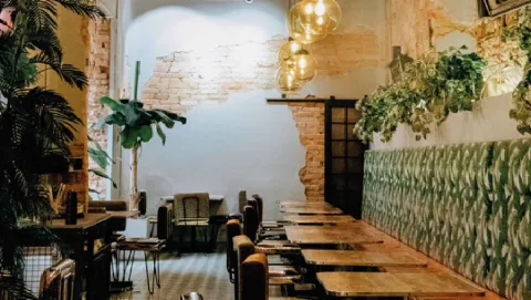 Comedor con paredes de ladrillo expuesto, plantas tropicales, lámparas esféricas y banquetas tapizadas en verde.
