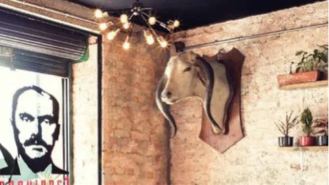 Pared de ladrillo con la cabeza decorativa de un animal, una lámpara araña moderna y un retrato en la entrada.
