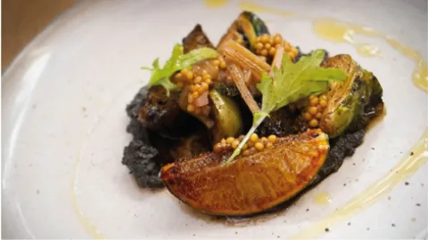 Un plato de verduras asadas, incluyendo coles de Bruselas y cebollas, servido en un plato de cerámica con una salsa oscura.