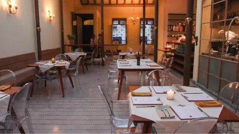 Una mesa de madera rústica en un salón de restaurante, con platos de cerámica, copas de vino y una vela encendida.