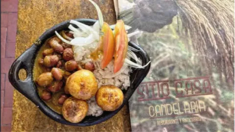 Cazuela de barro con fríjoles, arroz blanco, papas criollas, rodajas de tomate y cebolla junto a la carta.