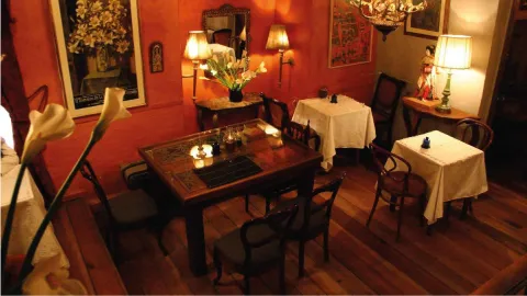 Vista superior de un salón con paredes rojas, suelo de madera, mesas vestidas e iluminación tenue de lámparas.
