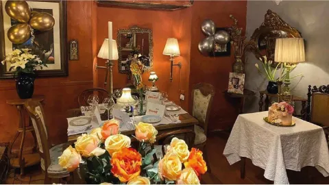 Salón decorado para celebración con globos dorados y plateados, arreglos de rosas, pastel y mesas vestidas.