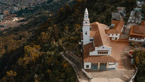 Vista aérea de la iglesia de Monserrate, rodeada por el bosque y con Bogotá extendiéndose al fondo.