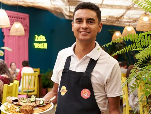 Mesero sonriente presenta un plato de comida, en el colorido y acogedor ambiente interior del restaurante.