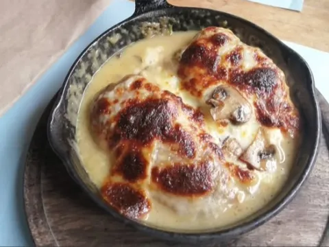 Plato de pollo gratinado con champiñones, servido en una sartén de hierro.