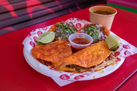 Variedad de tacos y quesadillas de birria acompañados de salsas y limón.