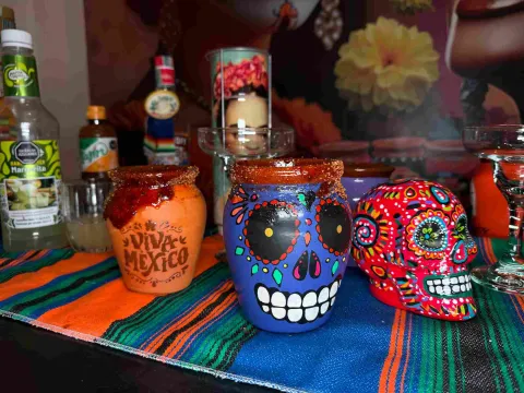 Vasos de barro decorados con motivos mexicanos y bebidas tradicionales, junto a coloridas calaveras.