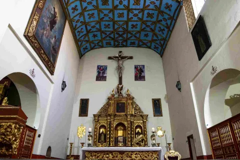 Altar lateral de la Iglesia de San Juan de Dios, con un elaborado retablo dorado, imágenes religiosas y un techo de madera decorado en tonos azules.