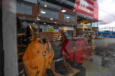 El escaparate de una tienda deportiva en Floresta Outlet exhibe prendas y calzado para actividades al aire libre, mientras el reflejo del exterior permite apreciar el movimiento de la calle, los vehículos y el transporte público frente al establecimiento.