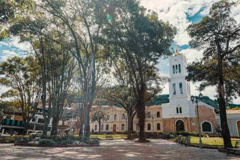 La Plaza de Usaquén, rodeada de árboles, jardines y bancas, con la iglesia de Santa Bárbara como uno de sus principales referentes arquitectónicos.