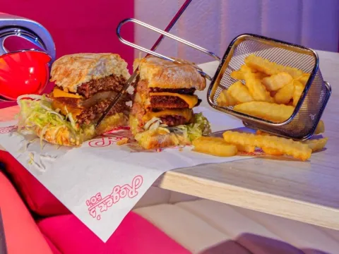 Hamburguesa artesanal doble con queso, lechuga y salsas, acompañada de papas crocantes en estilo clásico.