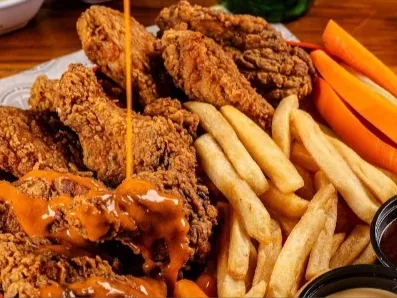 Alitas de pollo crujientes con salsa, acompañadas de papas fritas y bastones de zanahoria, servidas en una bandeja.