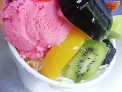 Ensalada de frutas con helado de fresa, mango, kiwi y chocolate, acompañada de coco rallado.