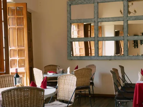 Salón de restaurante con decoración cálida, mesas dispuestas para los comensales, sillas de mimbre, puertas de madera y grandes espejos que amplían el espacio.