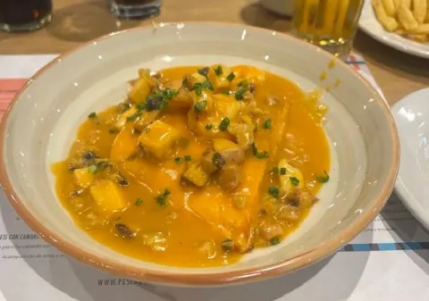 Plato de mariscos en salsa cremosa, acompañado de papas y decorado con hierbas frescas.