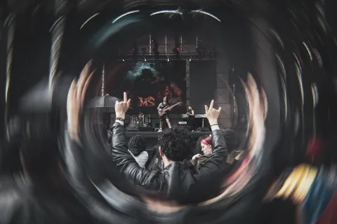 Público en concierto de rock levantando las manos frente al escenario, visto a través de un efecto circular que resalta la energía del momento.